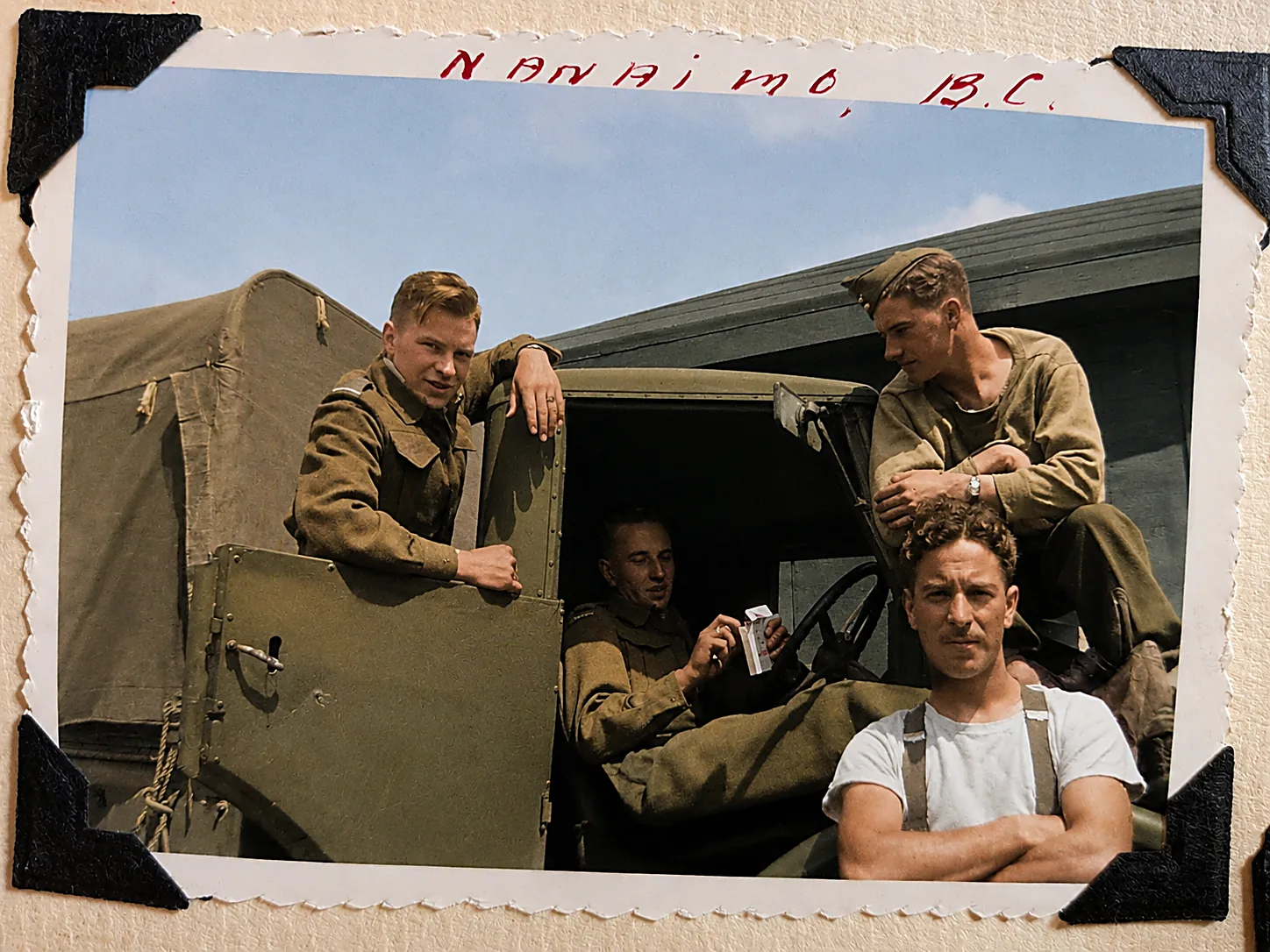 Colourised photograph of four young soldiers on and around an army truck in the summer sun, one in a white singlet with arms folded. Caption reads Nanaimo, B.C.