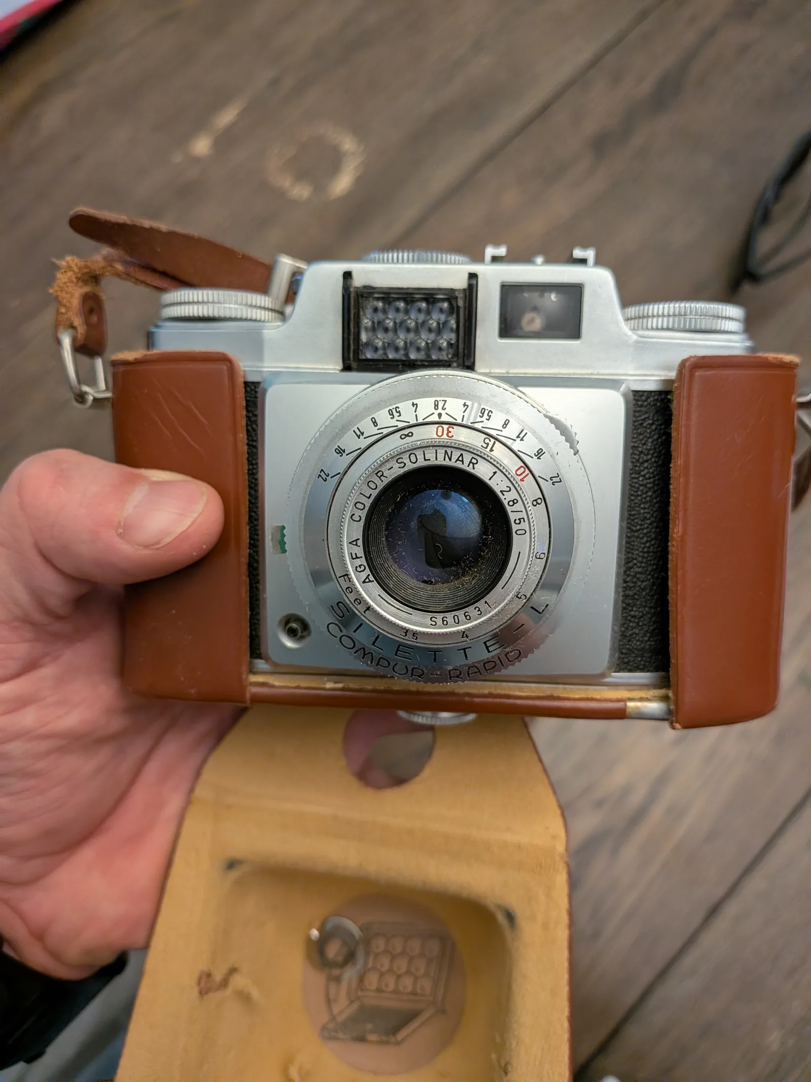 A West German Agfa Silette-L camera in its worn leather case, held in one hand over a wooden table — my great-grandfather's camera.